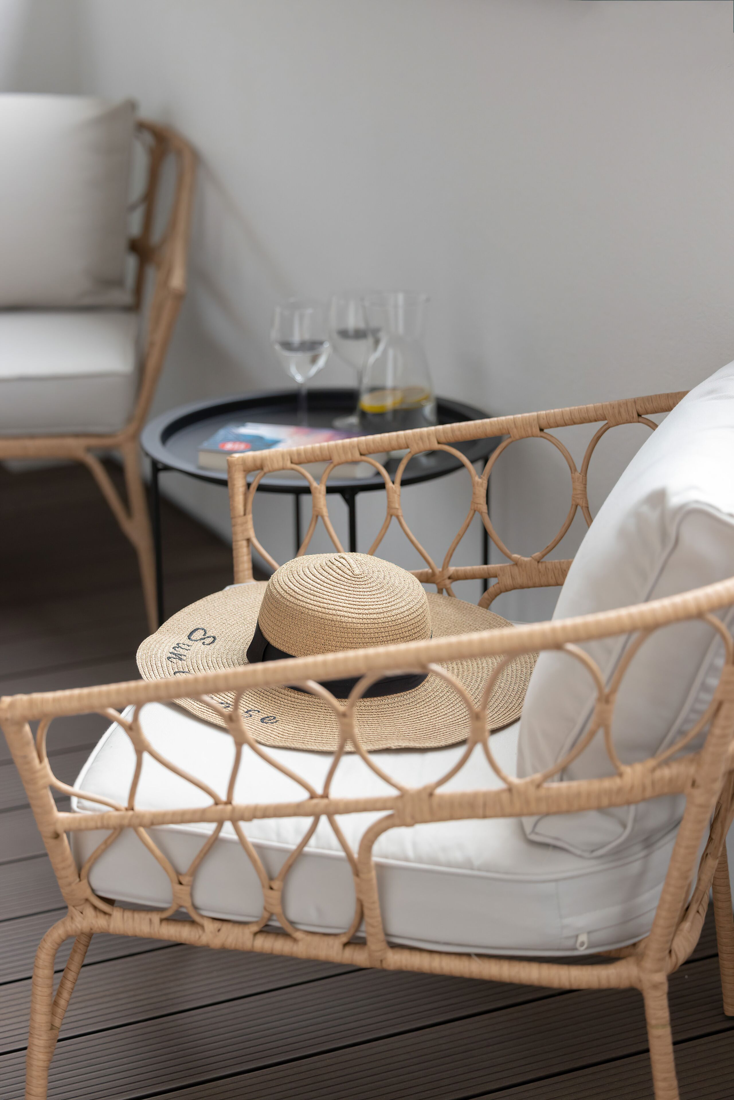 Wicker furniture with a white cushion, a wicker chair, and a wicker table with two glasses and a book.