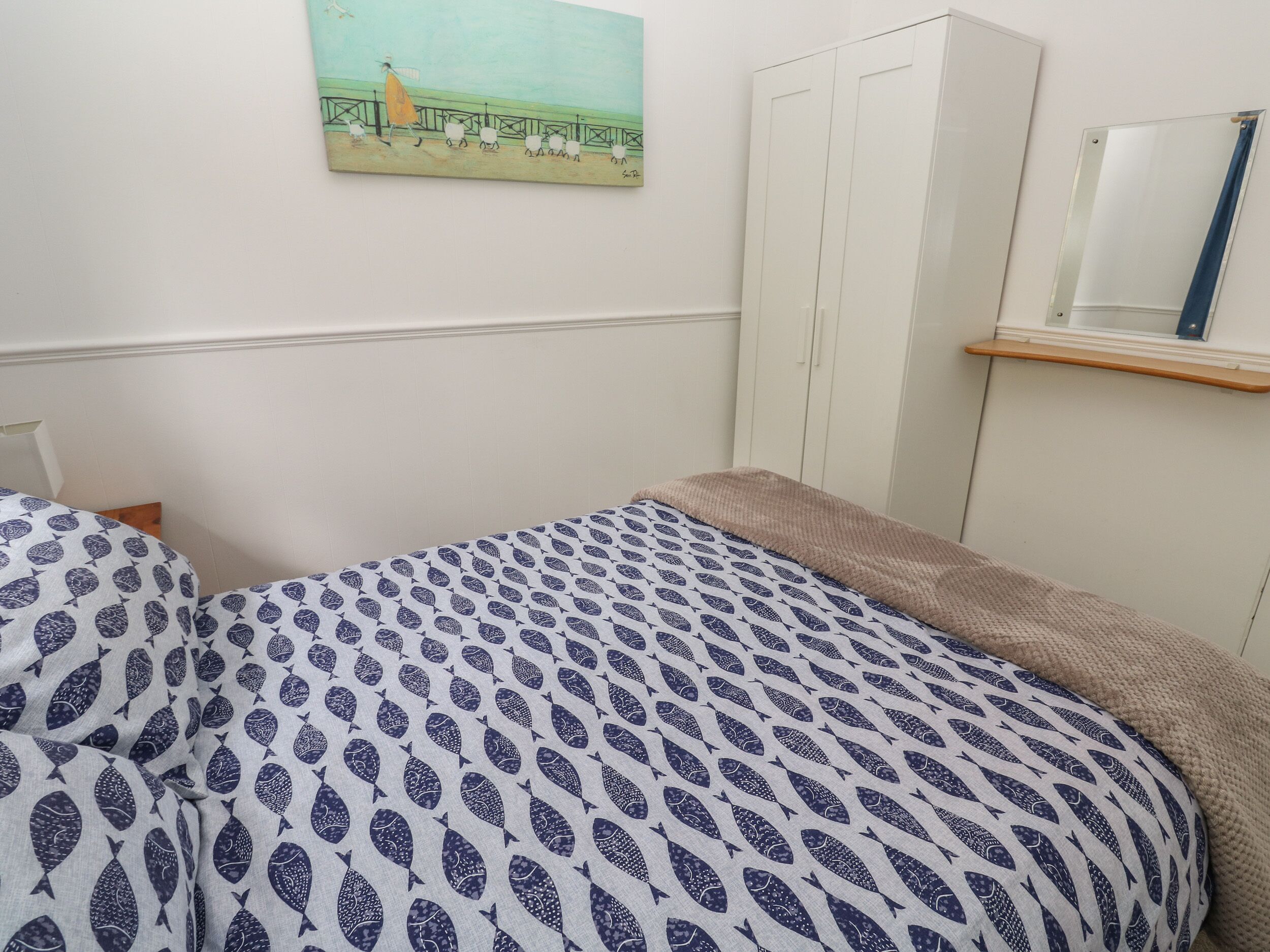A bedroom with a bed, a wardrobe, a painting, and a mirror.