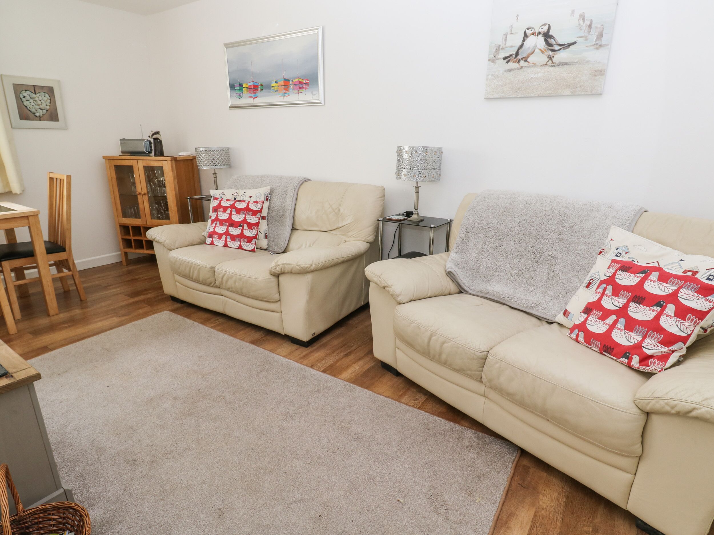 A living room with two beige sofas, a wooden cabinet, a small table, and a lamp.