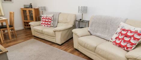 A living room with two beige sofas, a wooden cabinet, a small table, and a lamp.