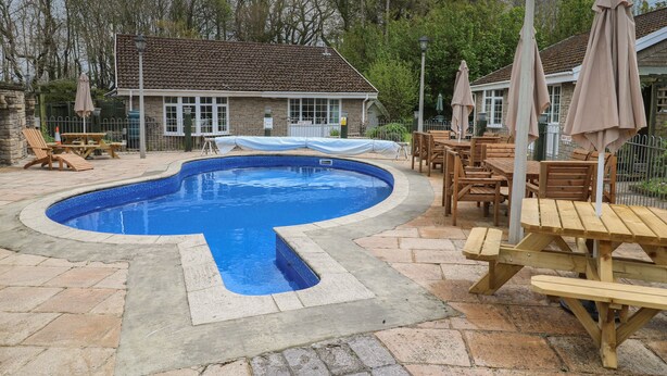Une piscine à la forme originale, entourée de carreaux de pierre et agrémentée de mobilier en bois.