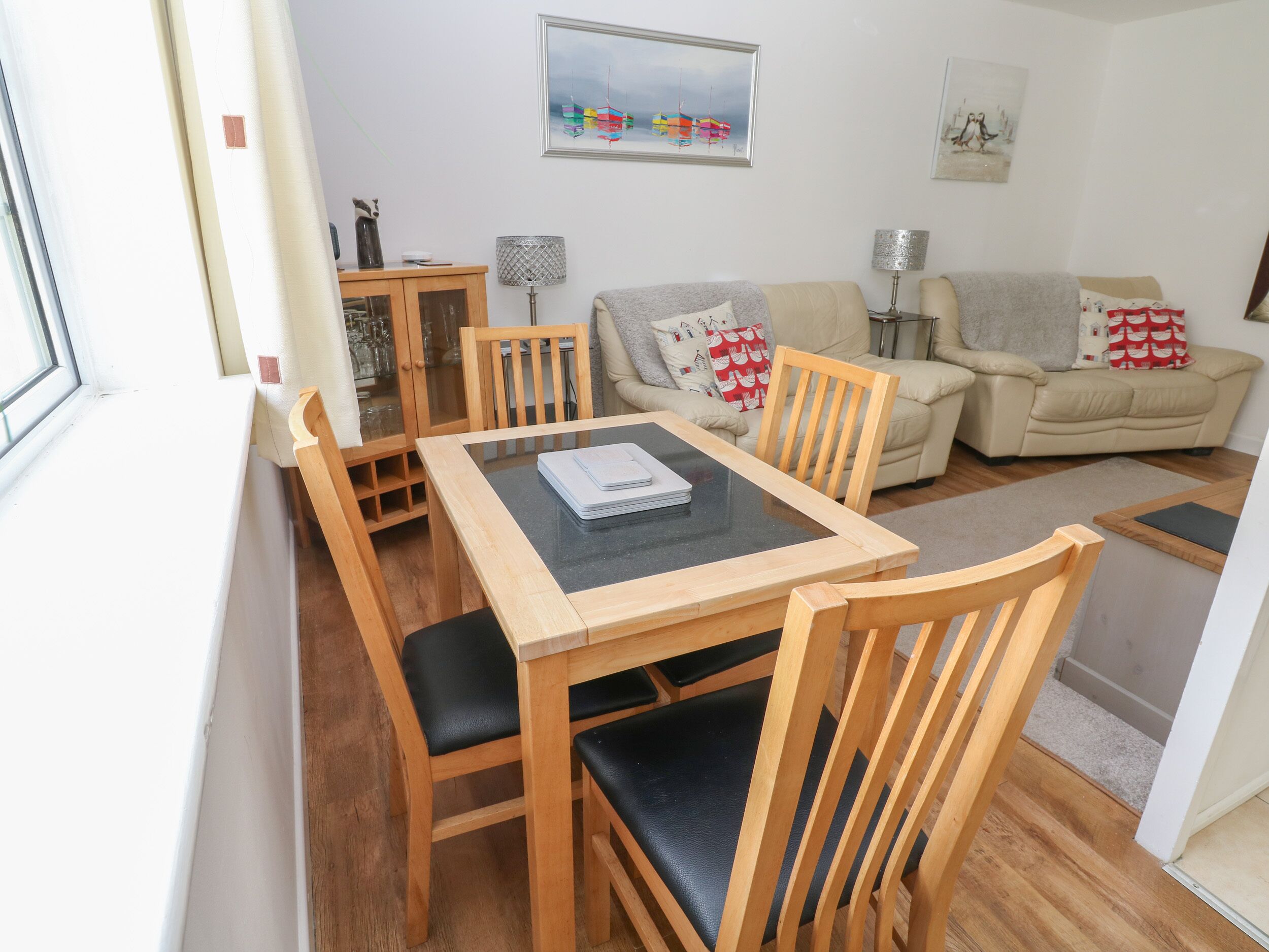 Ein gemütliches Wohnzimmer mit einem Holzesstisch, zwei Holzstühlen, einem beige gefärbten Sofa und einem kleinen Beistelltisch mit einer Lampe.