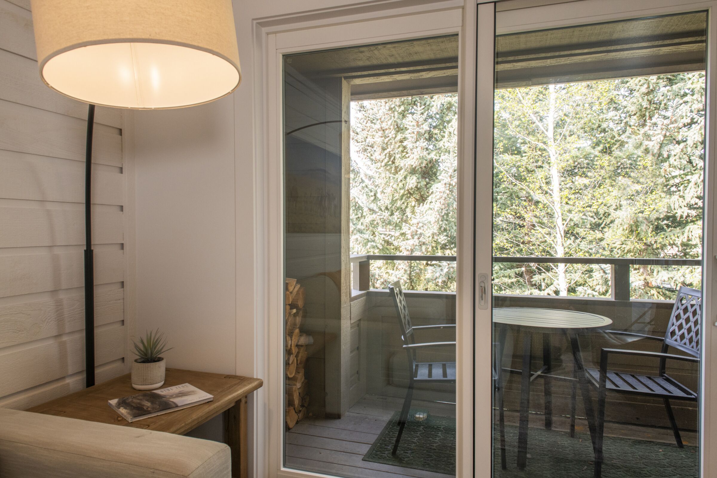 Une pièce avec un banc en bois, une petite table ornée d’une plante et une porte vitrée donnant sur un espace extérieur équipé d’une table et de chaises.