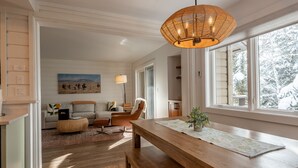 Una sala de estar moderna con una mesa de centro de madera, un sofá y un sillón. Hay un cuadro en la pared y una ventana con vistas a árboles.