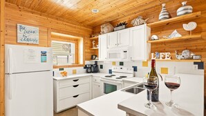A modern kitchen with white cabinetry, a built-in oven, microwave, and a coffee maker. There are decorative items on the shelves and a sign on the wall. - Bron's Beach Shack with Pool & Near Beach (Port Aransas)