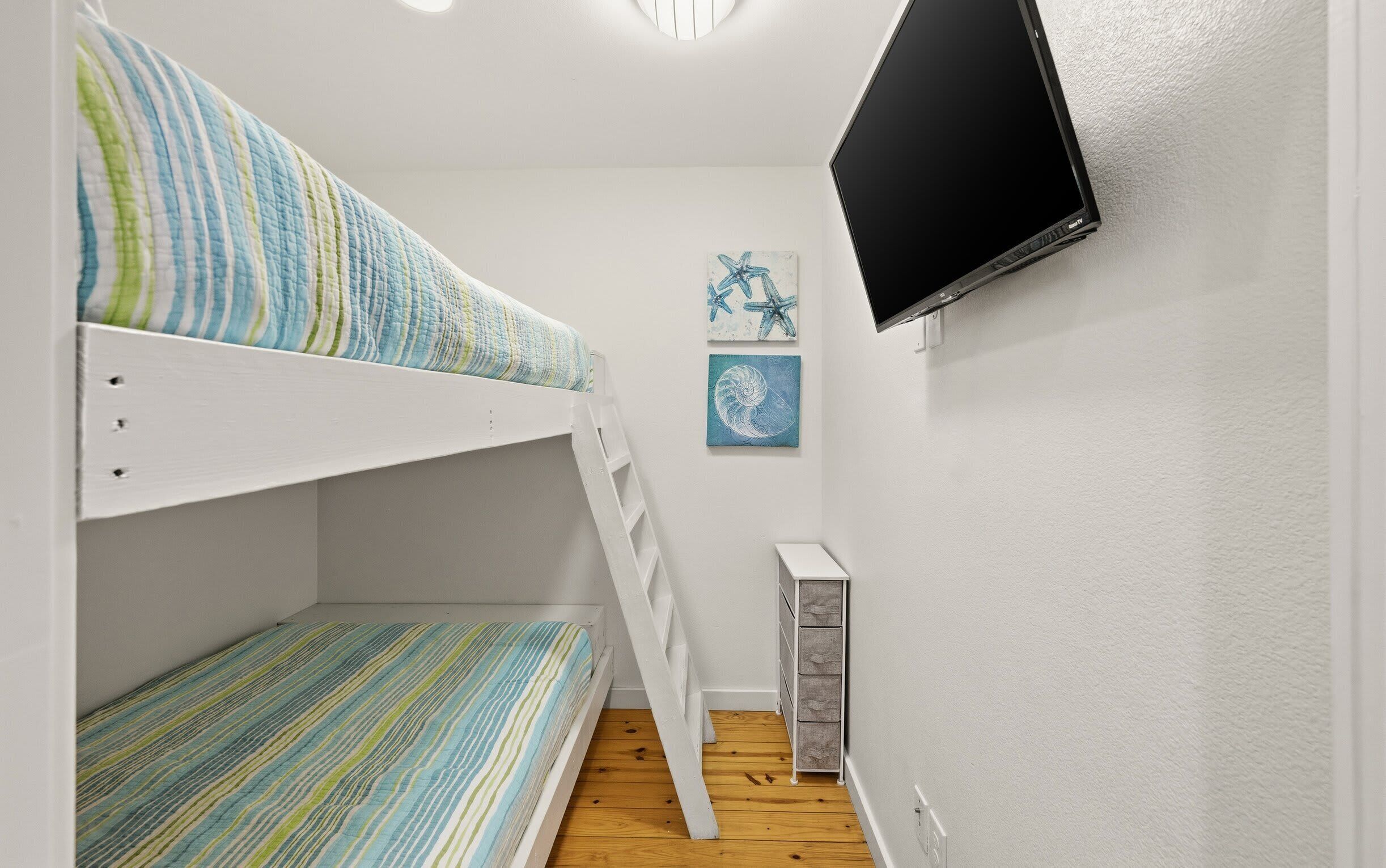 Een slaapkamer met een stapelbed, een televisie aan de muur, een ladder en een klein kastje.