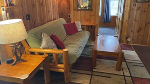 A cozy cabin interior with a wooden sofa, a table, and a lamp. - Kettle Cove in Sebago Lake, Maine (Casco)