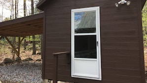 A small cabin with a white-framed window, a wooden deck, and a metal roof vent. - Kettle Cove in Sebago Lake, Maine (Casco)