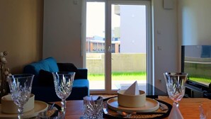 Ein Essbereich mit einem Tisch für zwei Personen, einer Couch und einem großen Fenster mit Blick auf ein Gebäude und Grünflächen.