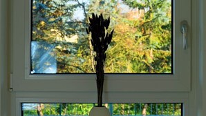 Ein Fenster mit Blick auf Bäume und eine weiße Vase mit Trockenpflanzen an der Fensterbank.