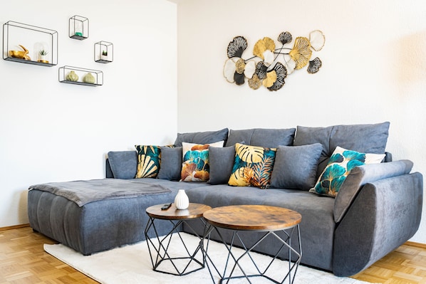Un salon moderne avec un canapé gris, des coussins colorés et un élément décoratif mural.