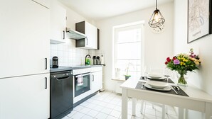 A modern kitchen with white cabinets, a dishwasher, an oven, and a dining area with a table set for two. - Zentral Gelegenes 55 m² Design-apartment (Magdeburg)