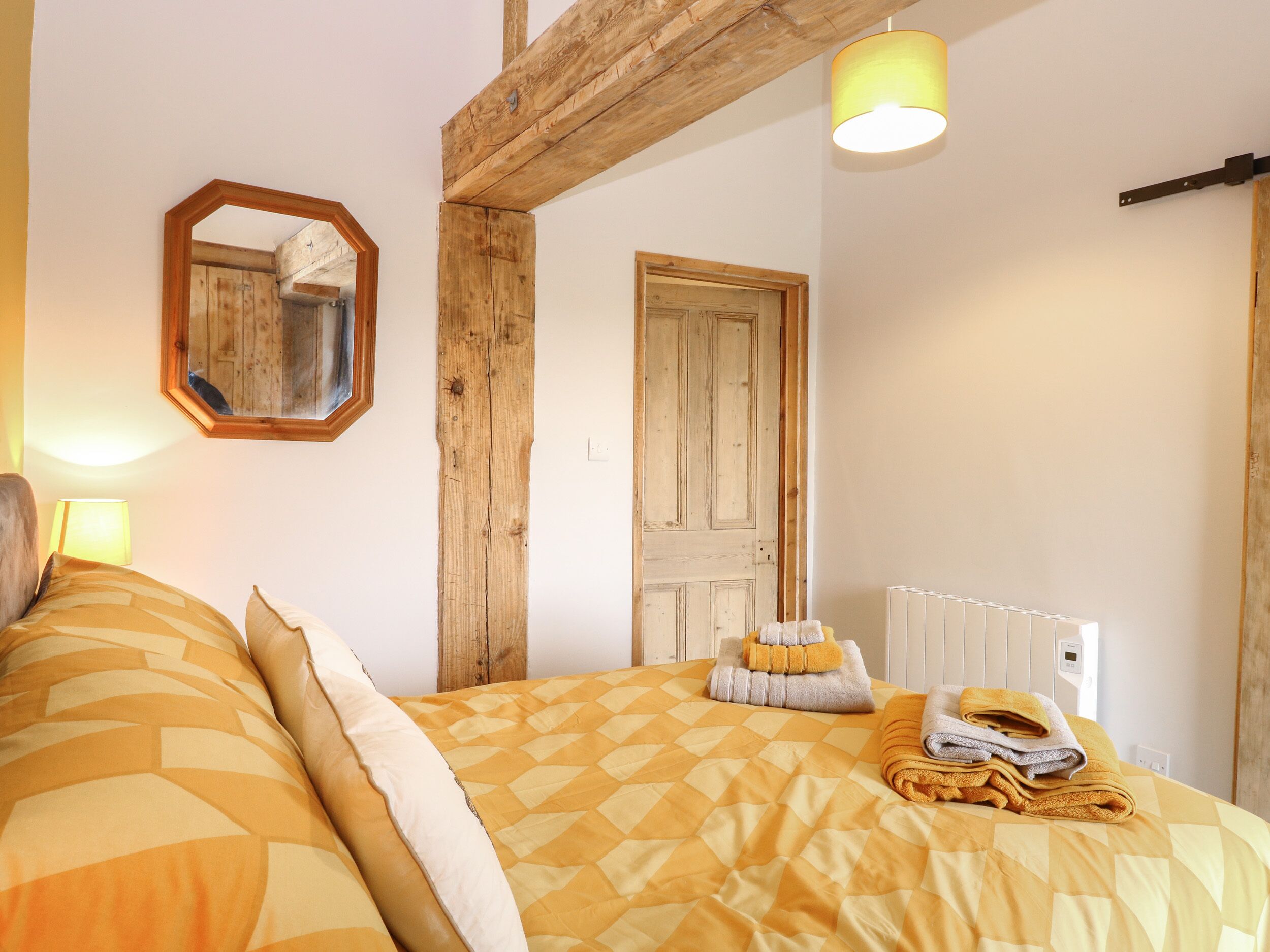 A bedroom with a bed, wooden beams, a mirror, a door, and a radiator.