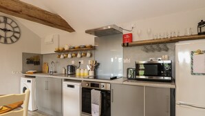 A modern kitchen with stainless steel appliances, a wooden ceiling beam, and a clock on the wall. - Bee Happy Barn (Norwich)