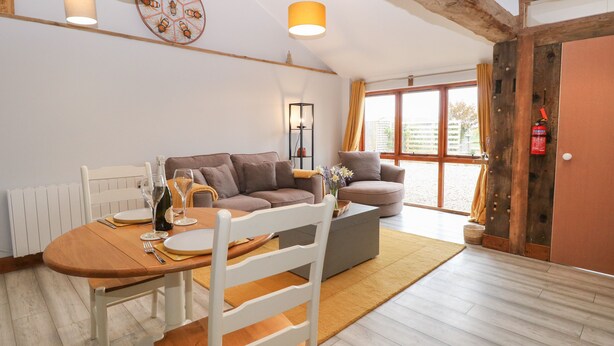 A modern living room with a dining area, featuring a sofa, a coffee table, and a dining table set for two. - Bee Happy Barn (Norwich)