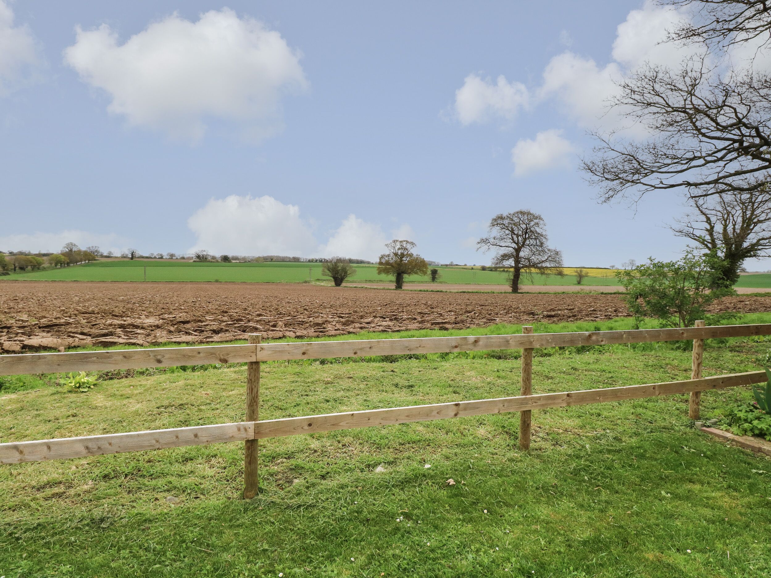 Un paysage rural avec un champ labouré, de l’herbe verte et des arbres sous un ciel dégagé.