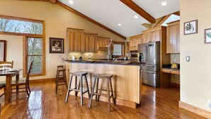 Una cocina amplia con armarios de madera, una isla grande con taburetes, un refrigerador y un ventanal que proporciona luz natural.