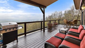 Una terraza techada al aire libre con una parrilla, mobiliario de mimbre y vistas del paisaje.