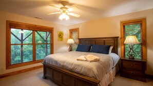 Un dormitorio con una cama grande, ventilador de techo y dos ventanas con persianas.