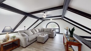 A loft bedroom with a large L-shaped sectional sofa, a wooden coffee table, and a small side table with a lamp.