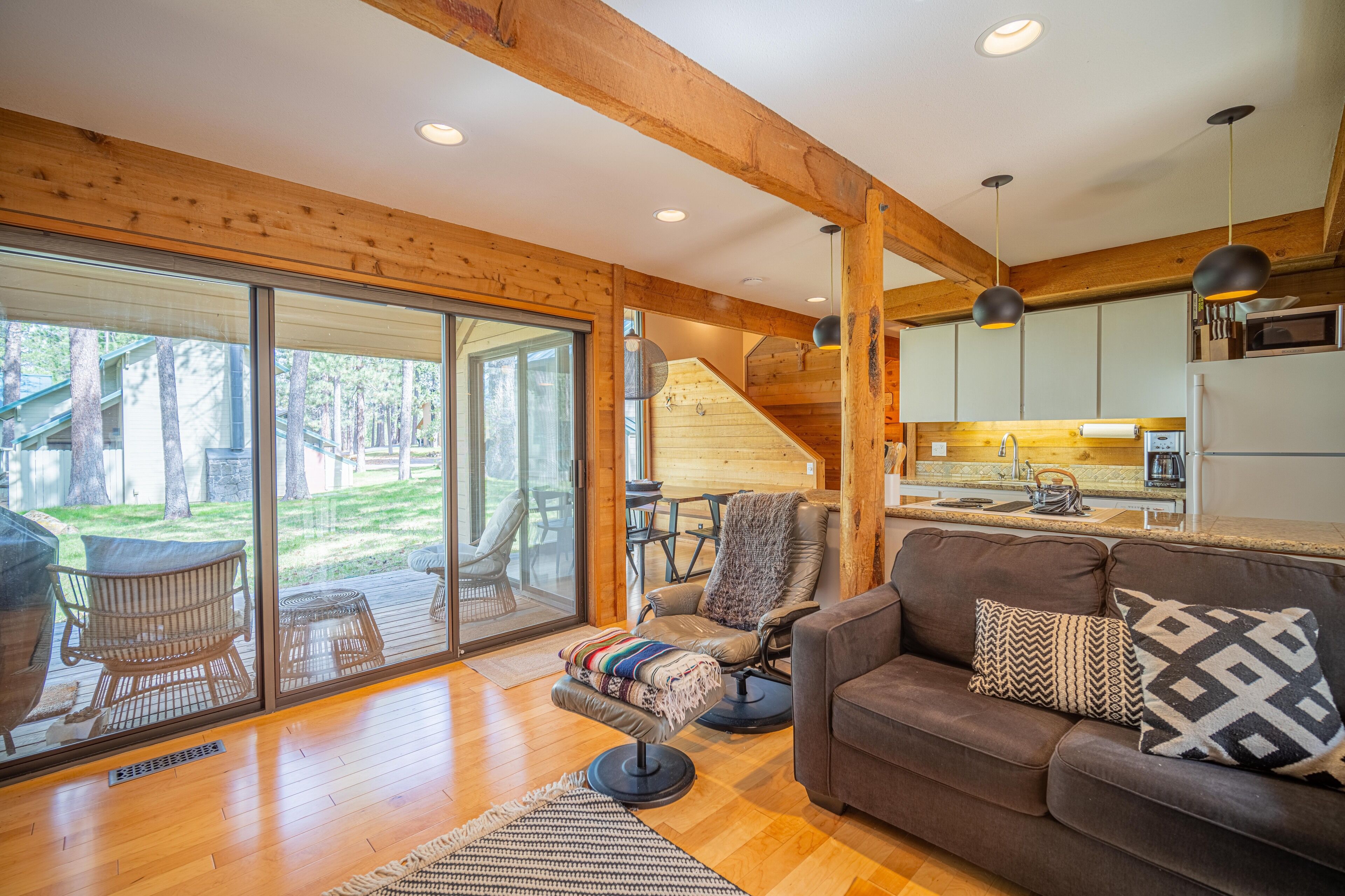 A spacious living area with a wooden floor, a brown sofa, and a large sliding glass door leading to a patio.