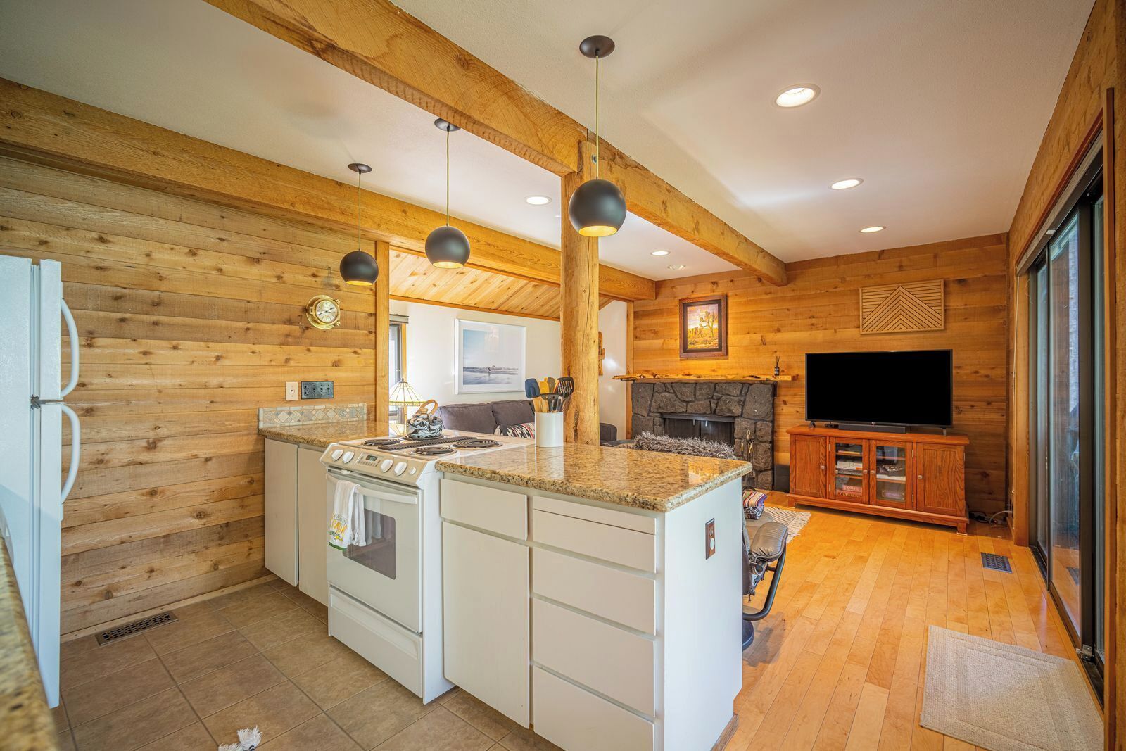 A kitchen with a central island, wooden walls, a stone fireplace, and a TV in a wooden cabinet.