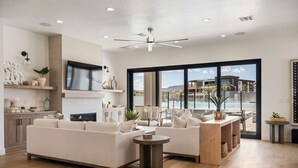 A spacious living room with a large sofa, a coffee table, and a dining area with a view of a pool and mountains. - The Beach Front 2.0: Private Pool, Lagoon + Beaches (St George)
