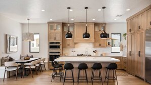 A modern kitchen with wooden cabinets, a central island with bar stools, and pendant lighting. - The Beach Front 2.0: Private Pool, Lagoon + Beaches (St George)