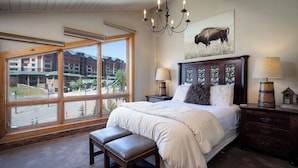 A bedroom with a large window, a bed with a wooden headboard, two bedside tables with lamps, and a bench.