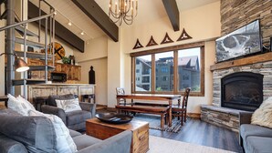 A modern living room with a fireplace, a dining area, and a view of a snowy landscape through large windows.
