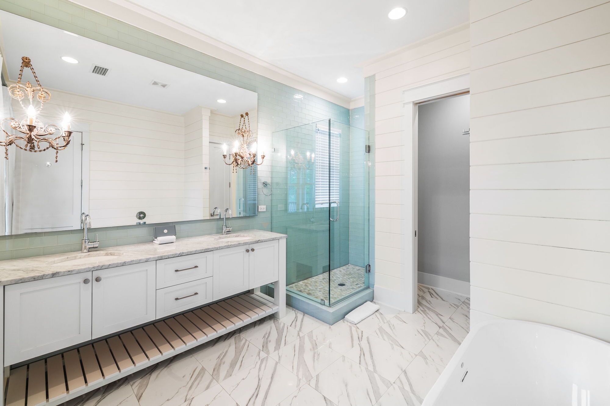 A modern bathroom with a marble floor, a glass-enclosed shower, a large mirror, and a white bathtub.