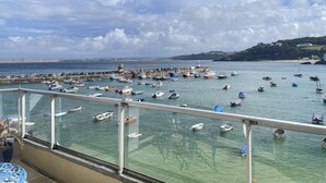 Un port où divers bateaux sont amarrés à un quai, un phare et une vue sur la côte.