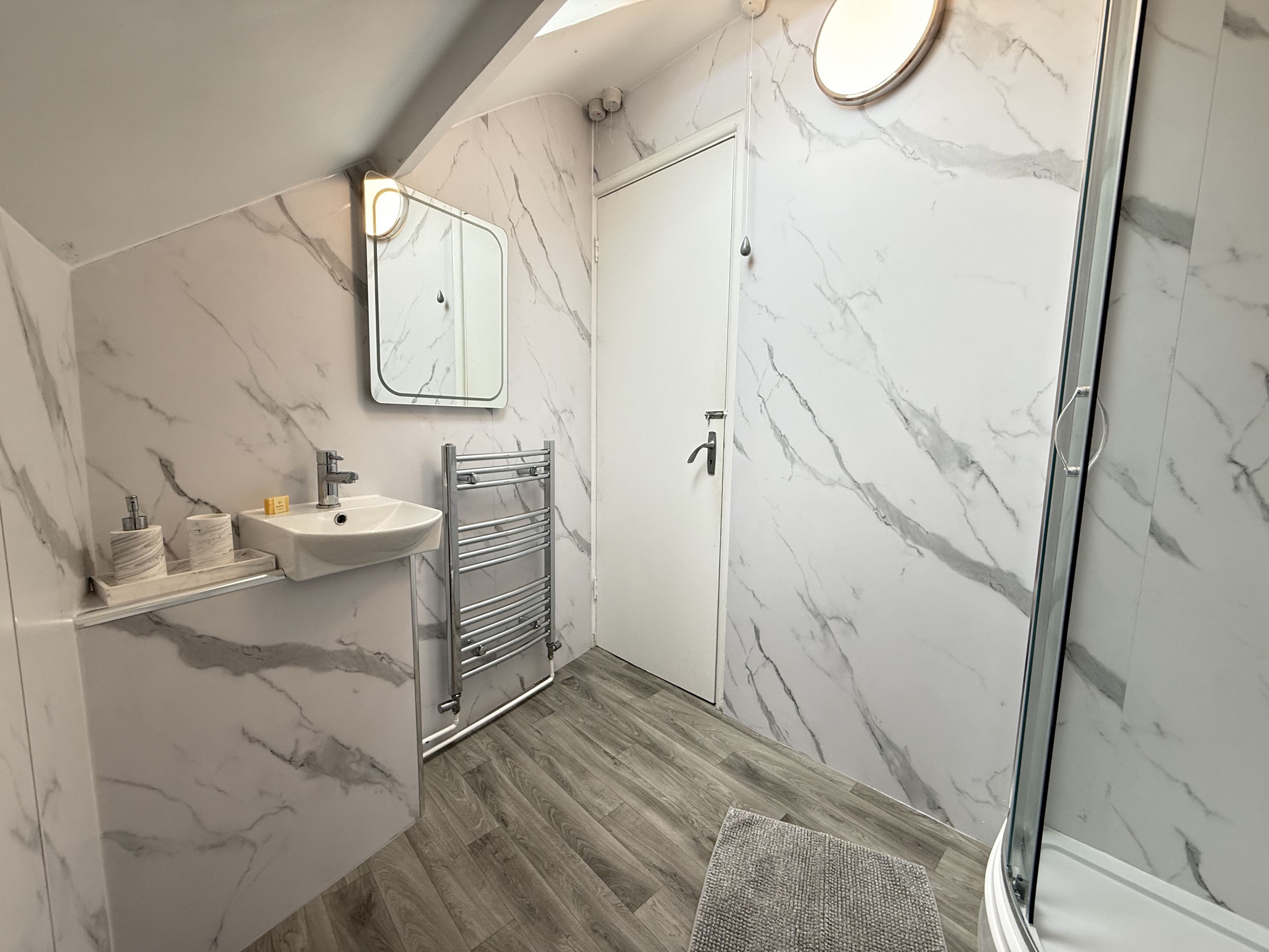 A bathroom with a marble wall, a sink, a towel rack, and a shower area.