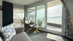 Un salon moderne avec un canapé, un fauteuil et une vue sur la mer grâce à de grandes fenêtres.