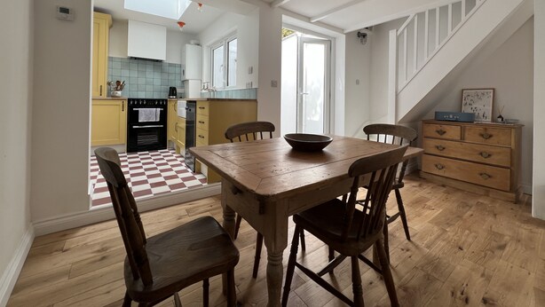 Un comedor con mesa y sillas de madera, una cocina al fondo y una escalera que sube a otro nivel.