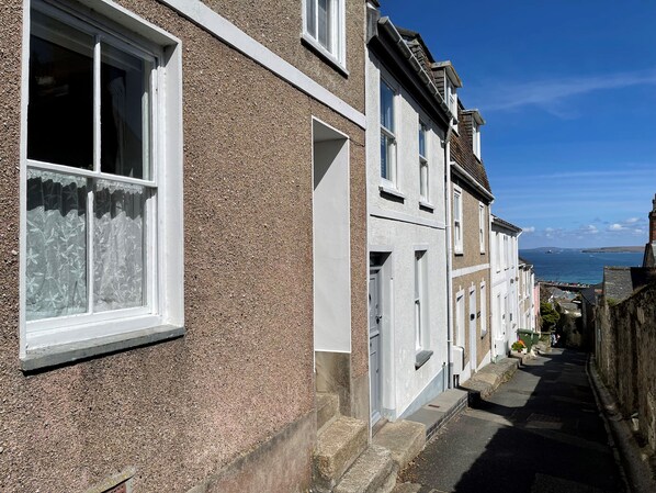 Eine schmale Straße mit Reihenhäusern, freie Sicht auf das Meer und eine entfernte Insel.