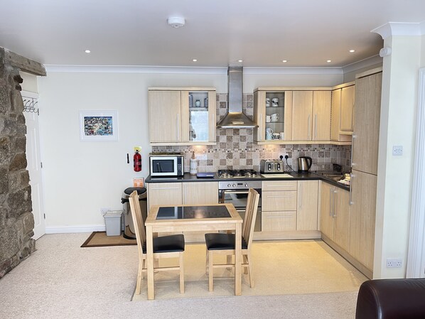 A modern kitchen with wooden cabinets, a gas stove, a microwave, and a toaster. - Penryn a modern spacious ground floor apartment (St Ives)
