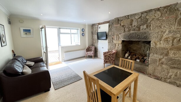 A living room with a stone fireplace, a sofa, a dining table with chairs, and a television mounted on the wall.