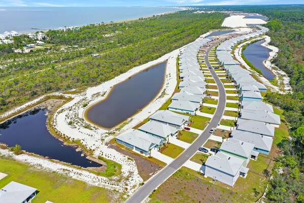 An aerial view of a residential area with houses arranged in a curved layout along a water body. - Large Single Level, 4BR with Lots of Entertainment in WindMark ~ Paradise Found (Windmark Beach)