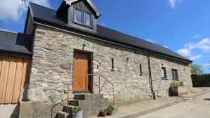 A stone cottage with a wooden door, a small porch, and a metal roof.