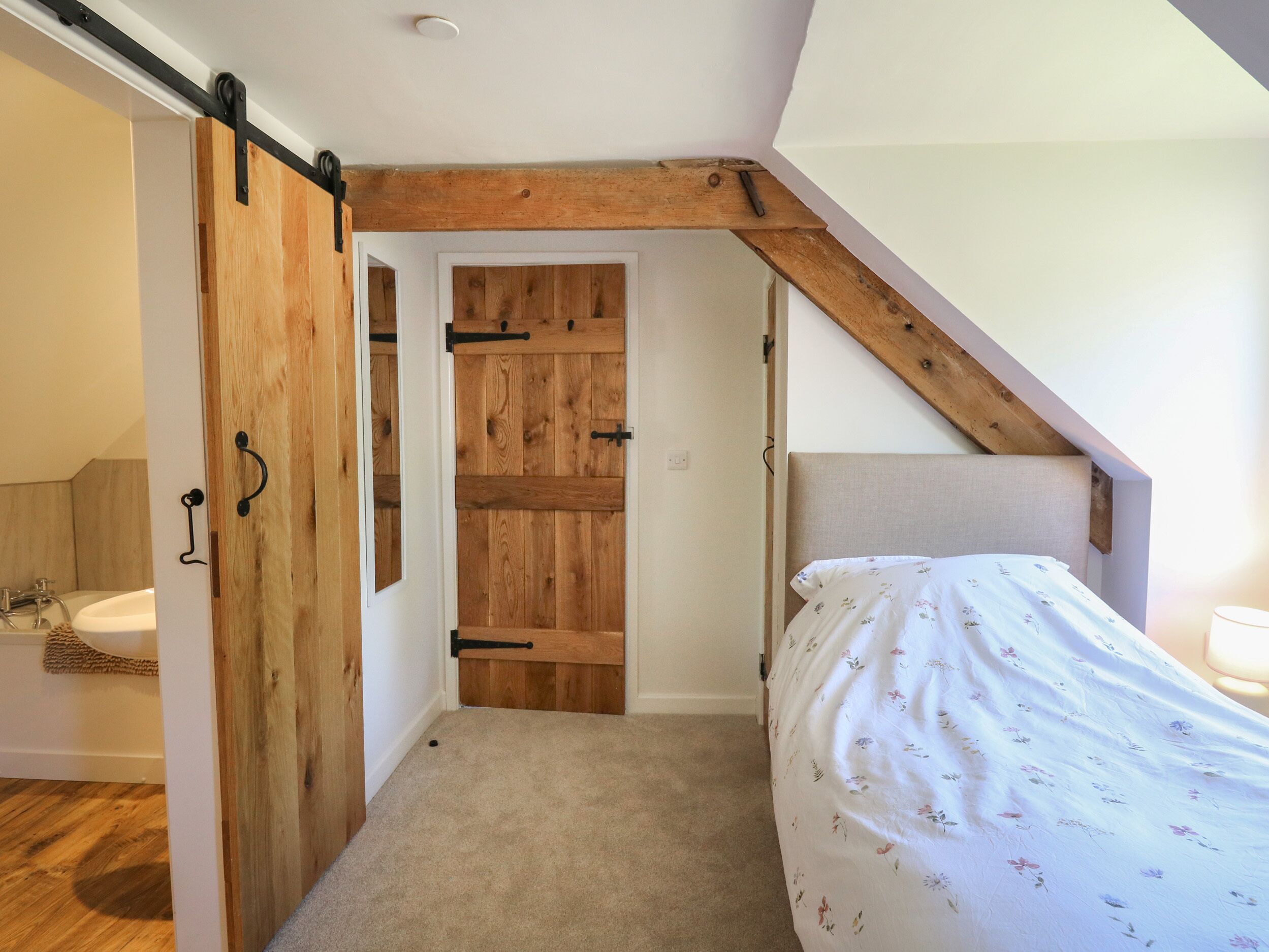 Un dormitorio con una puerta de madera, una cama con cubrecama floral y un techo inclinado.