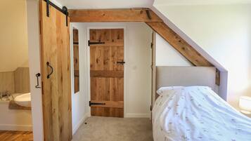 Un dormitorio con una puerta de madera, una cama con cubrecama floral y un techo inclinado.