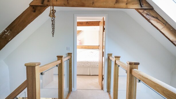 A narrow, wooden staircase with glass railings leading to a bedroom with a bed and a window.