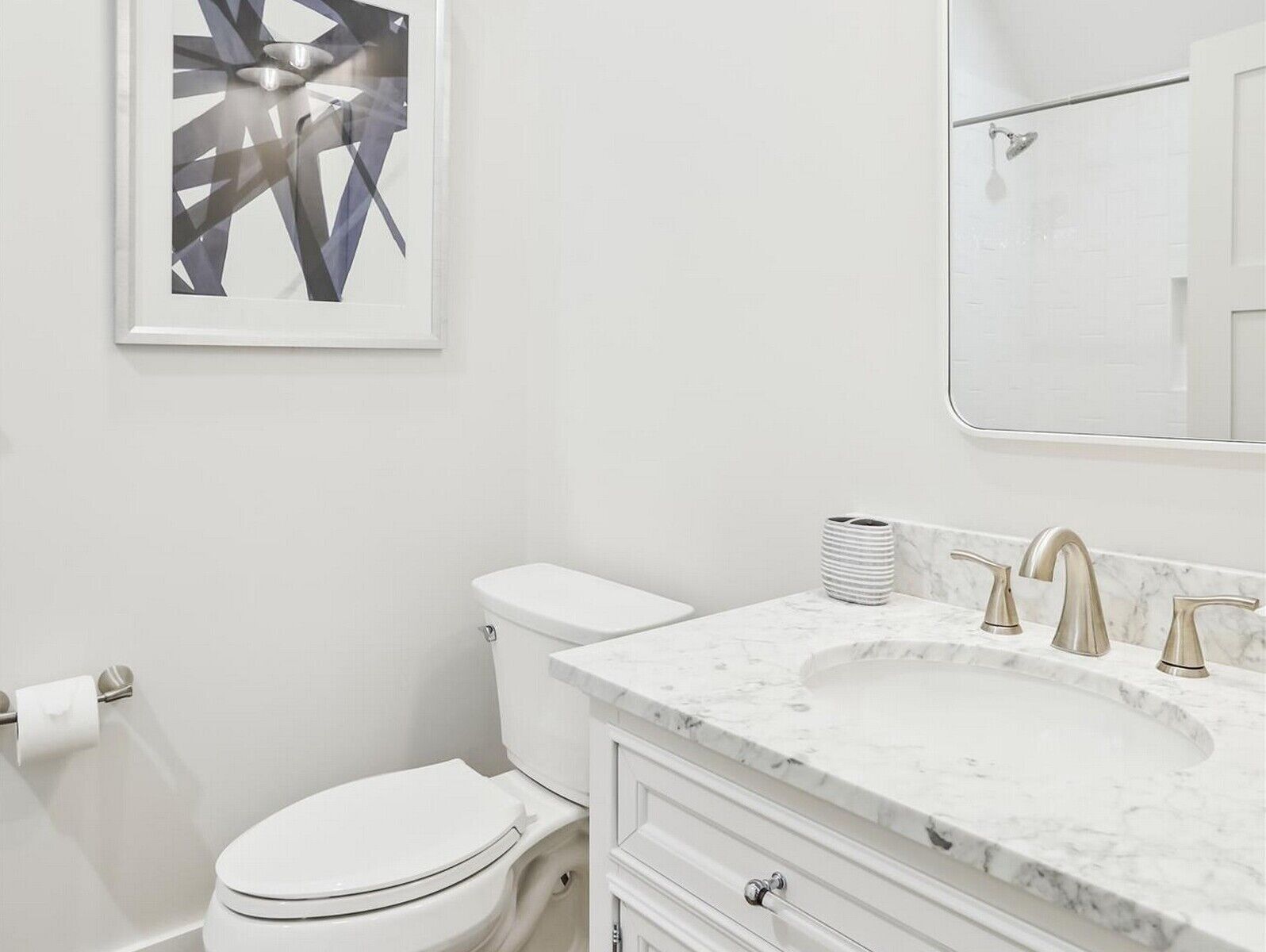 A modern bathroom with a white toilet, a marble sink, and a framed abstract artwork on the wall.