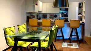 A modern kitchen with white cabinets, a stainless steel range hood, and a bar area with stools. - SUNSET (Cefalù)