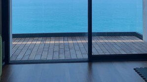 A room with a large sliding glass door leading to a wooden deck overlooking a calm sea. - SUNSET (Cefalù)