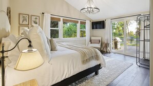 A bedroom with a large bed, a chandelier, a TV, and a view of the outdoors through a glass door.