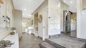 A modern kitchen with white cabinetry, a stainless steel refrigerator, and a stone-tiled entrance.