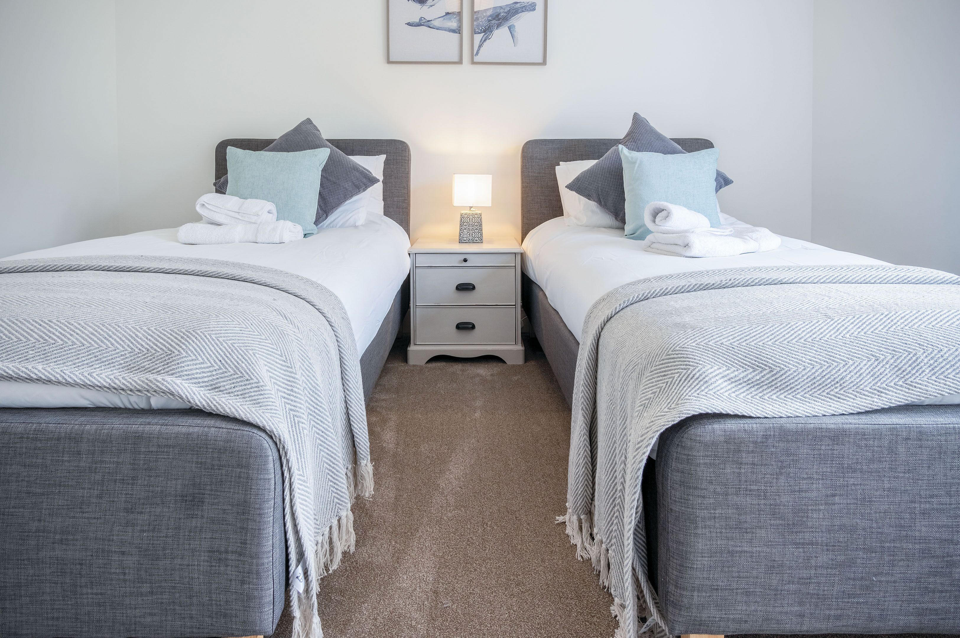 Une chambre double avec deux lits, chacun étant équipé d’un oreiller, d’une table de chevet avec une lampe et d’un petit tiroir.