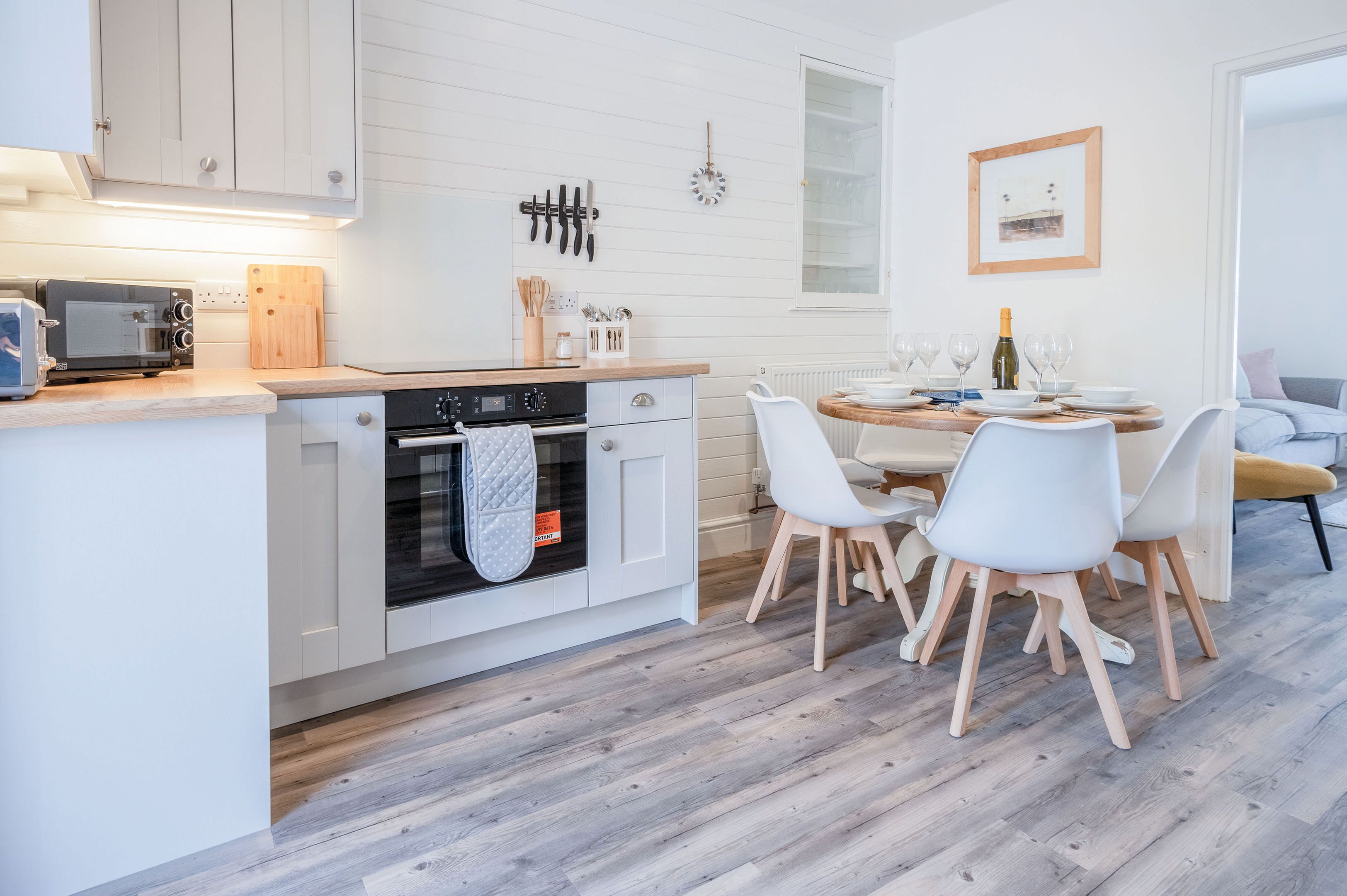 A modern kitchen with white cabinetry, a built-in oven, and a dining area with a round table and chairs.